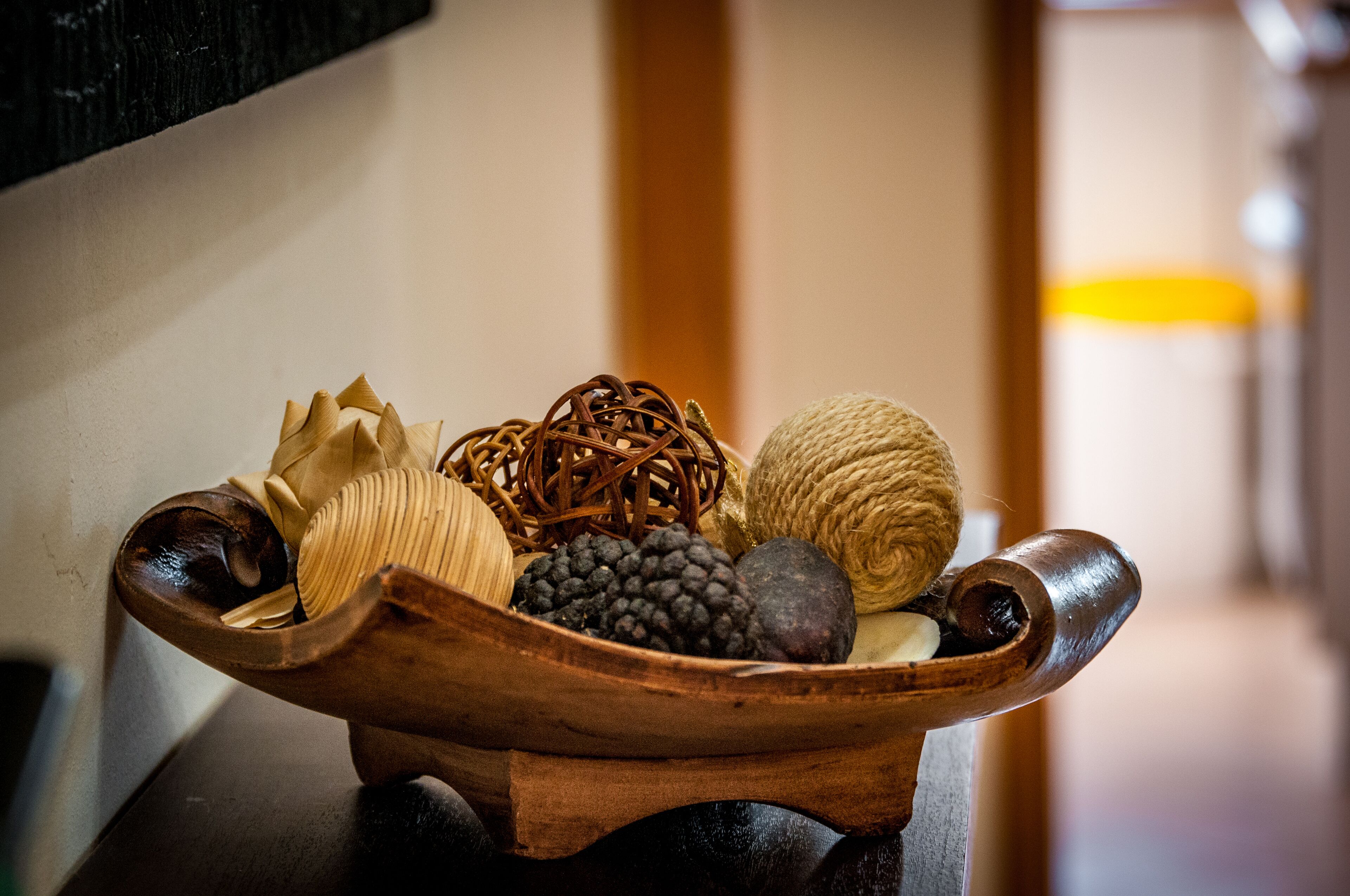 A wooden bowl filled with various items including a woven basket, a ball of twine, and several fruits.