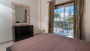 Quarto com cama, penteadeira, espelho, janela com cortinas e vista para o exterior.