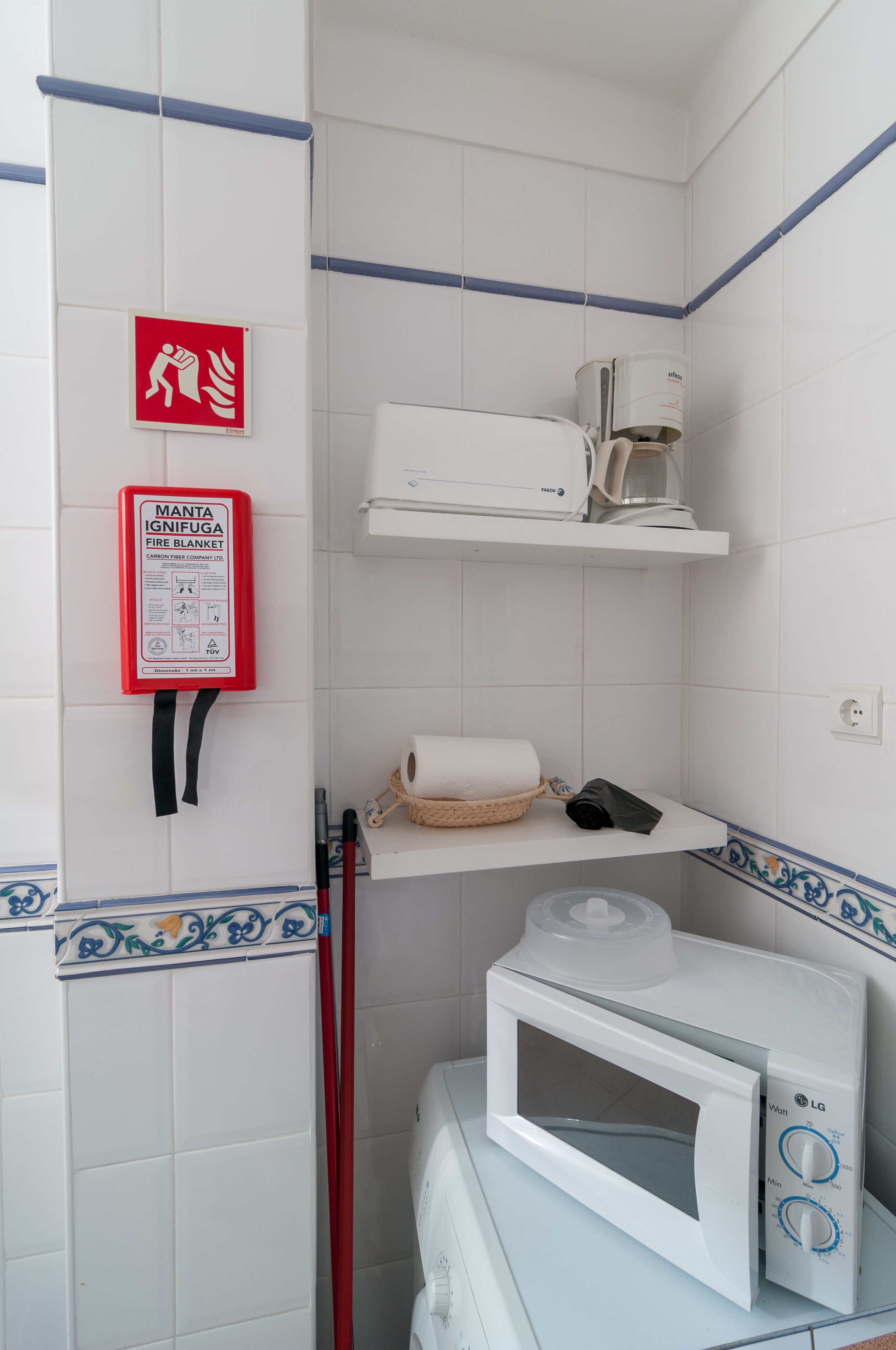 A bathroom with a white microwave, a white coffee machine, a fire blanket, and a red emergency exit sign.