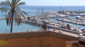 A marina with boats, a palm tree, and a lighthouse in the background.