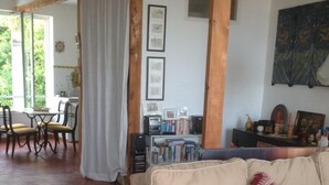 A cozy living room with a beige sofa, red patterned cushions, a wooden coffee table, and a bookshelf filled with books and decorative items.