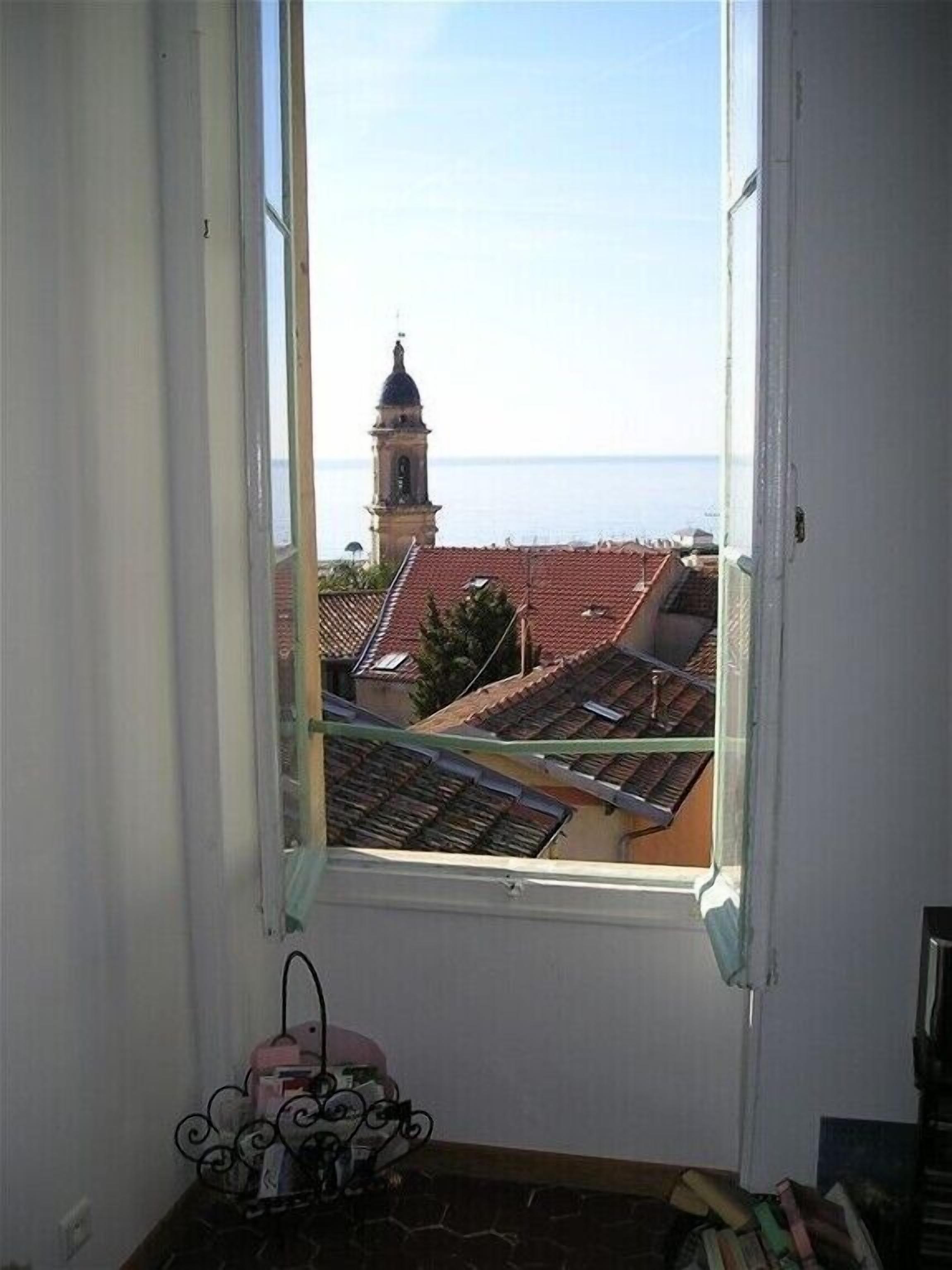 Et værelse med et vindue ud til en kystby, der viser et klokketårn og terracotta tagrender.