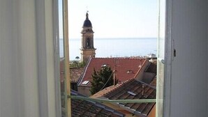 A room with a window overlooking a coastal town, featuring a bell tower and terracotta rooftops.