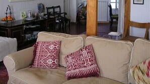 A living room with a beige sofa, wooden beams, a dining area with a table and chairs, and artwork on the walls.