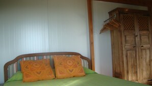 A bed with a striped bedspread and two orange pillows, a wooden wardrobe, and a wooden ceiling.