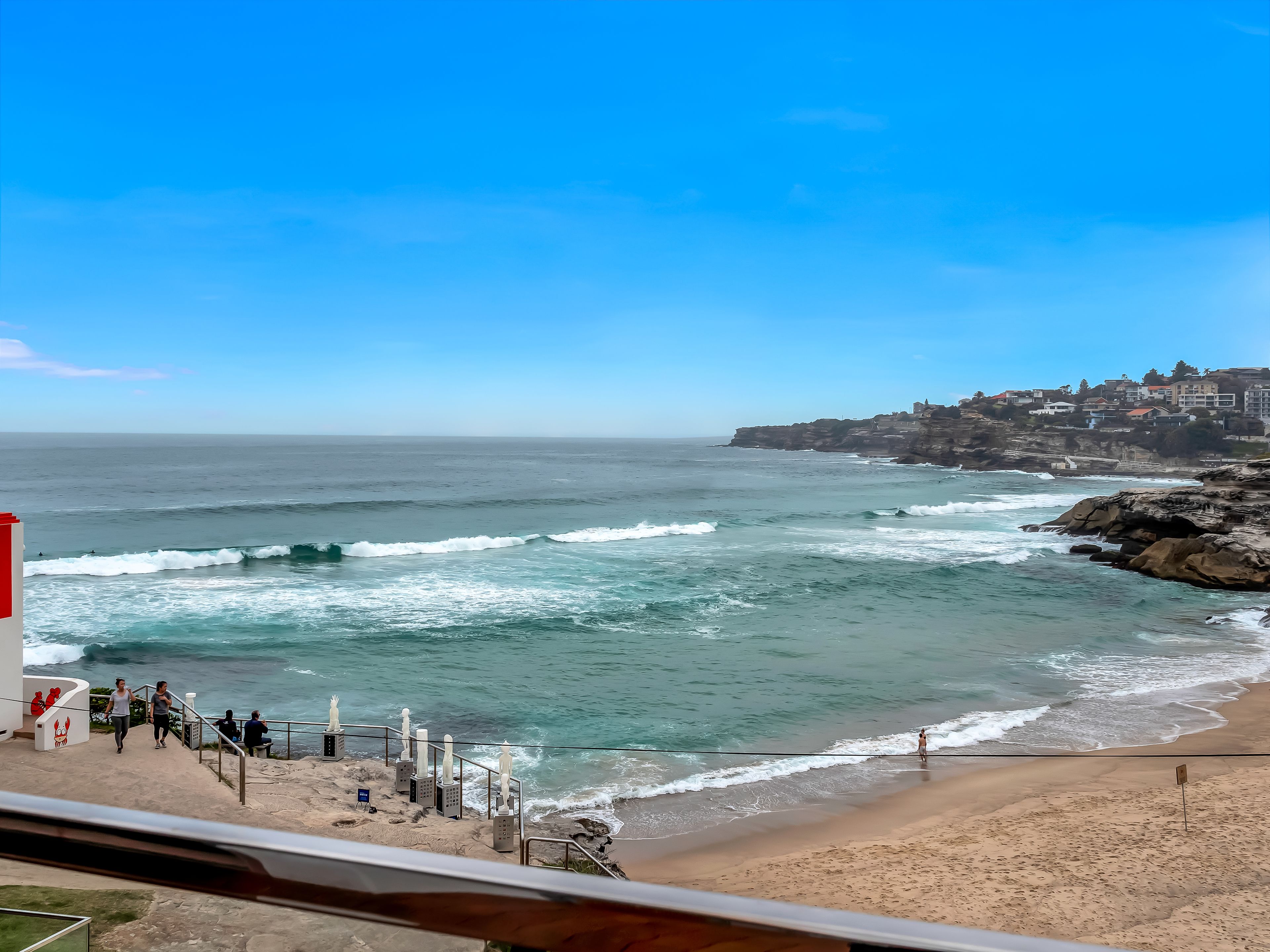 Vista costera con playa, olas y un pueblo en un acantilado.