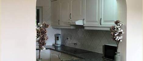 A kitchen with white cabinets, a granite countertop, and two vases with dried flowers.