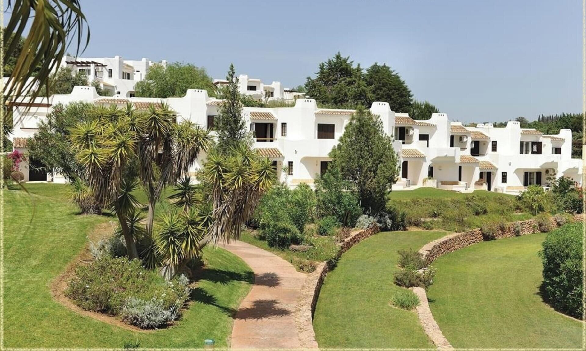 A residential area with white buildings, palm trees, and a pathway.