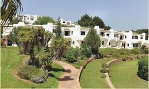Un bâtiment blanc doté de nombreux balcons, entouré de jardins bien entretenus et de palmiers.