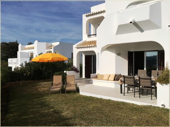 Une villa blanche dotée d’un patio, d’un espace salon extérieur et d’un parasol jaune.