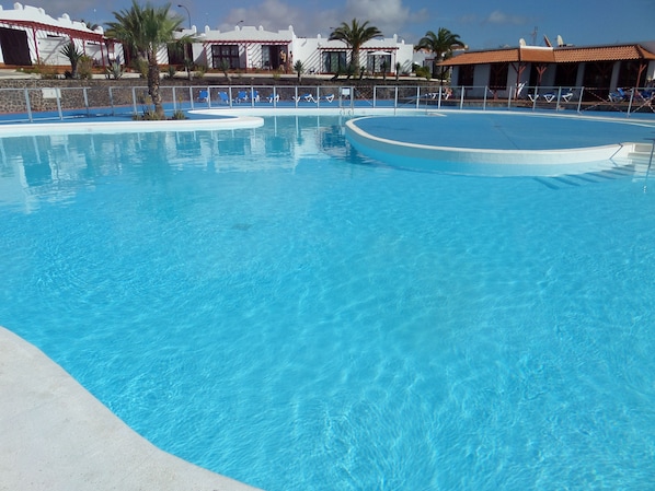 Une piscine d’un bleu éclatant, de forme incurvée, entourée d’un petit muret en pierre et de palmiers.