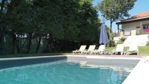 Une piscine à l’eau d’un bleu cristallin, entourée de chaises longues blanches et protégée par un parasol.