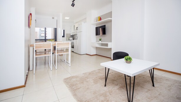Een moderne keuken met witte kasten, een eethoek met een witte tafel en een woonruimte met een bank en een televisie.