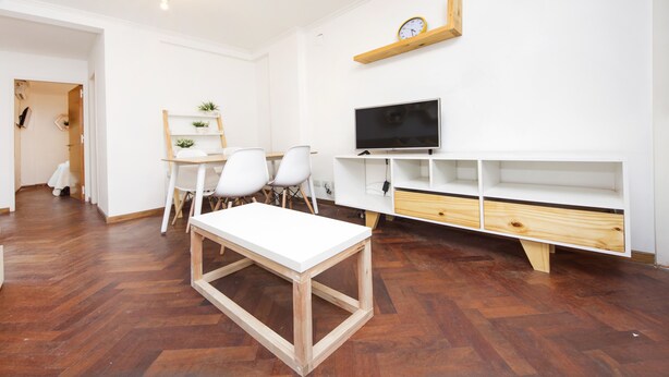 Uma sala de estar moderna com uma mesa branca, cadeiras, uma TV e estantes embutidas.