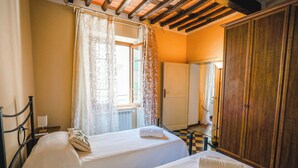Une chambre avec deux lits, une armoire en bois, un radiateur et une fenêtre avec des rideaux.