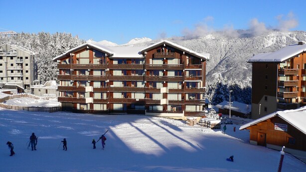 A multi-story hotel with a wooden facade, located in a snowy mountainous area with ski slopes visible. - Apartment with three genuine bedrooms within 2 mins walk of the main lift (Morillon)