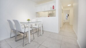 Une cuisine moderne avec des meubles blancs, une table à manger en verre et quatre chaises blanches.