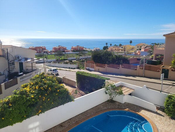 A residential area with a swimming pool, a view of the sea, and a white building with a balcony.