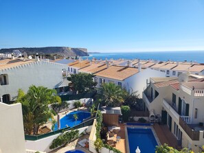 A residential area with terracotta-tiled roofs, a swimming pool, and a view of the sea.