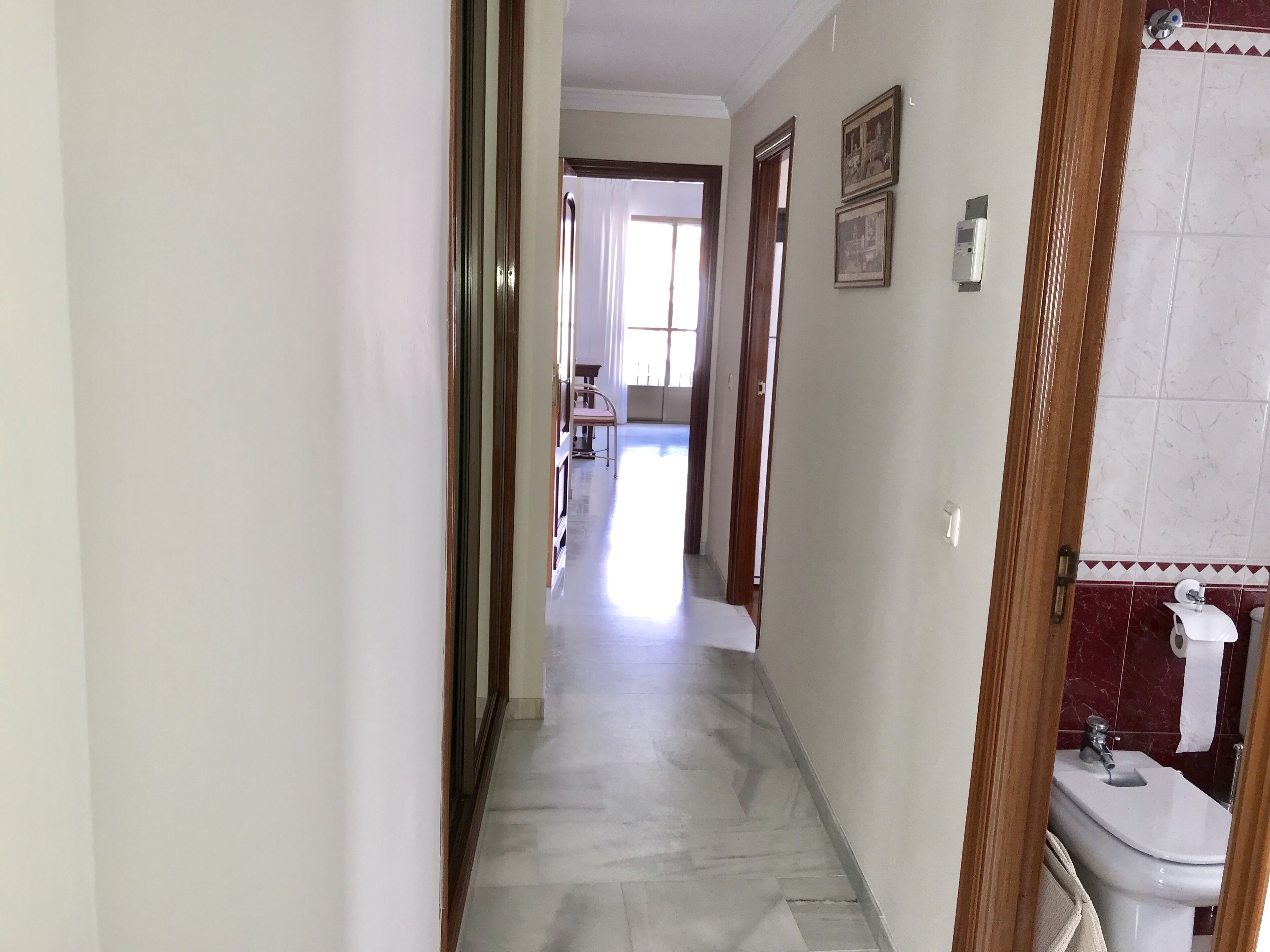 Un pasillo con suelo de baldosas que lleva a un baño con inodoro y lavabo.