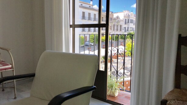 A room with a large window, a chair, and a view of buildings and a street outside.