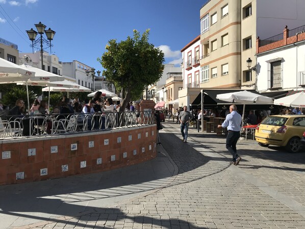 A cobblestone street with outdoor seating, a yellow taxi, and buildings with balconies.