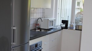 A modern kitchen with stainless steel appliances, white cabinetry, and a wooden floor.