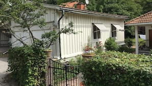 A white building with a satellite dish, a small porch, and a garden with various plants and flowers.