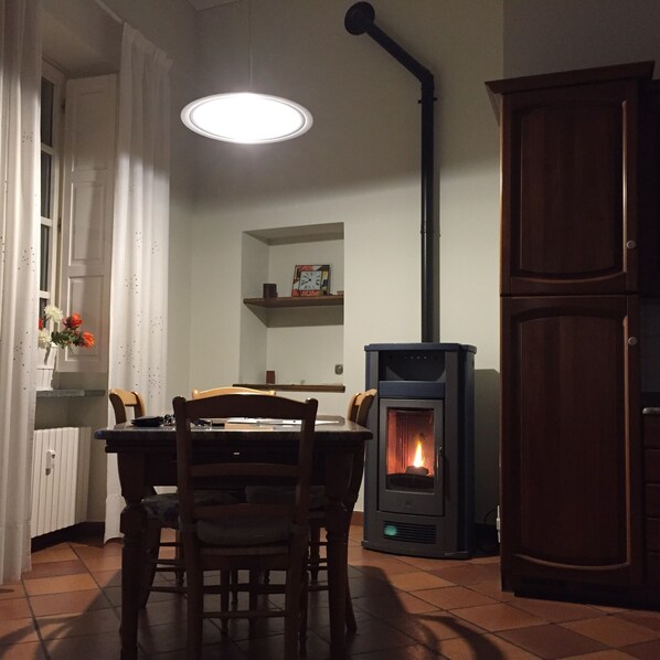 A dining area with a table, chairs, a pendant light, a wood-burning stove, and a cabinet.