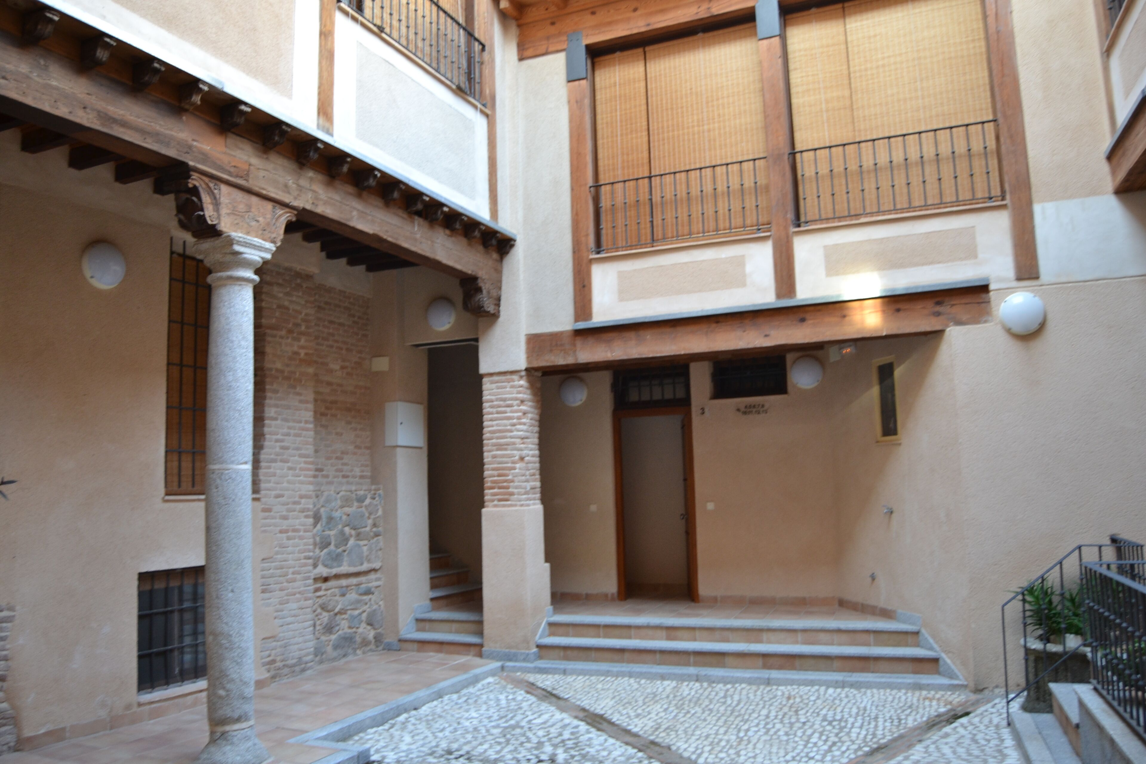 A courtyard with a stone floor, a wooden staircase, and a building with a balcony.