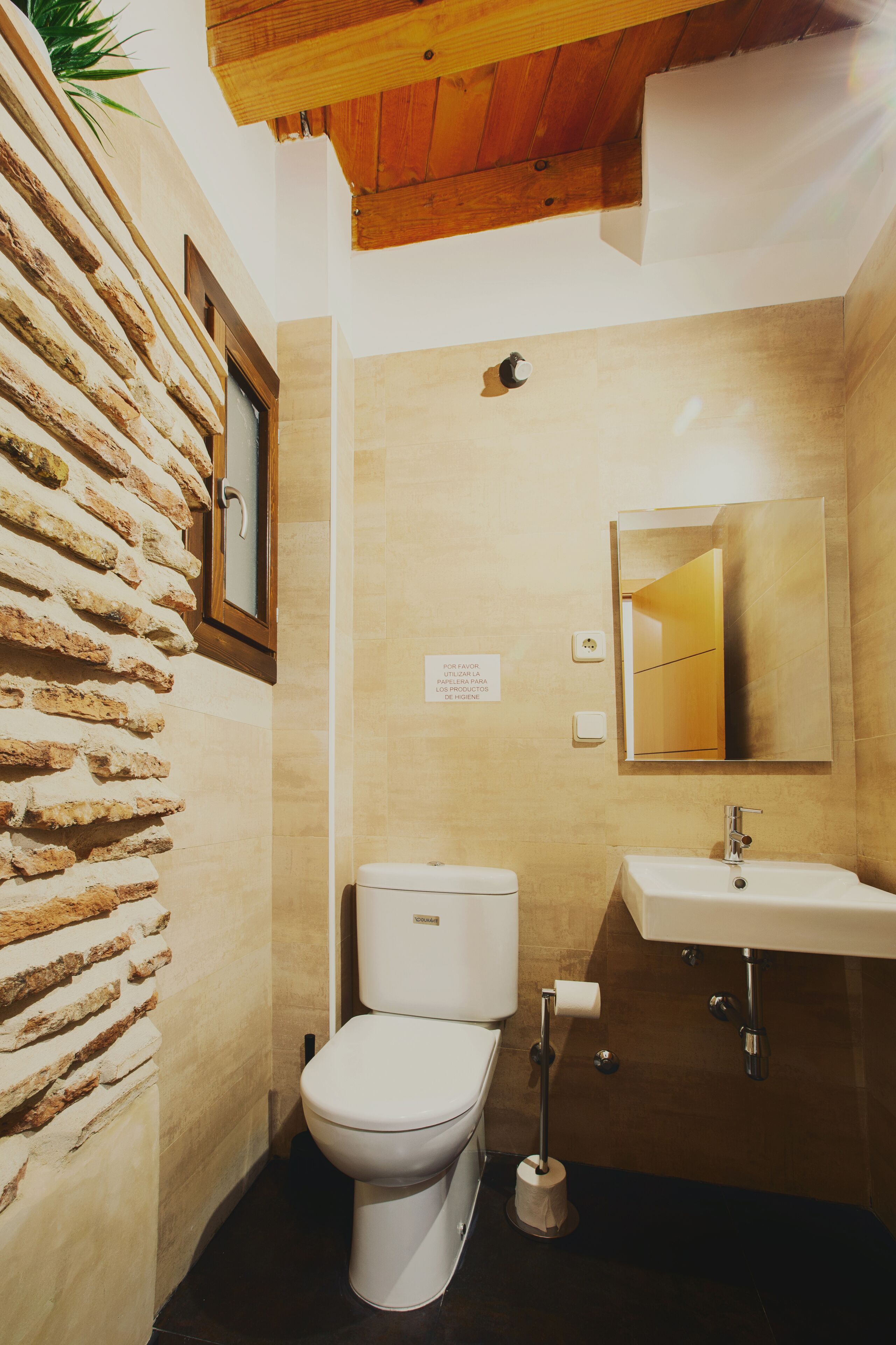 Een badkamer met een stenen muur, toilet, wastafel en spiegel.