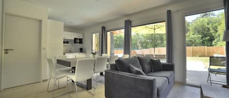 Un espacio de estar moderno con un sofá gris, sillas de comedor blancas y una zona de cocina.