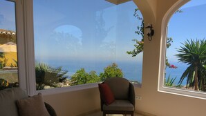 A room with a view of the sea, a sofa, a chair, and a table with decorative items. - 4 Bedroom Villa in Benalmadena Pueblo with pool and Magnificent Panoramic views (Benalmádena)
