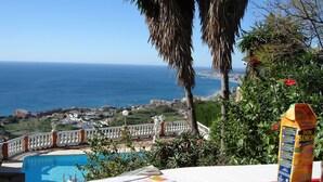 A poolside view with a newspaper, a cup, and a juice carton, overlooking a coastal cityscape. - 4 Bedroom Villa in Benalmadena Pueblo with pool and Magnificent Panoramic views (Benalmádena)