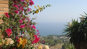 A balcony with vibrant bougainvillea flowers, a view of the sea, and a distant town. - 4 Bedroom Villa in Benalmadena Pueblo with pool and Magnificent Panoramic views (Benalmádena)