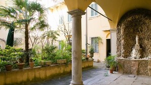 A courtyard with a palm tree, potted plants, a stone column, and a statue.