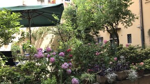 A courtyard with potted plants and flowers, a green umbrella, and a building in the background.