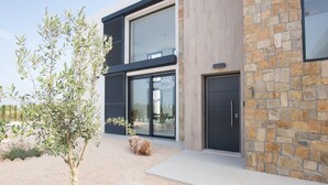 A modern building with a stone facade, large windows, and a gravel driveway. - Beachfront design villa in Bauhaus style, pool, highspeed internet, air conditioning / heating (Cala Murada)
