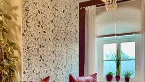 A room with a patterned wallpaper, a large window with potted plants, and two red leather chairs.