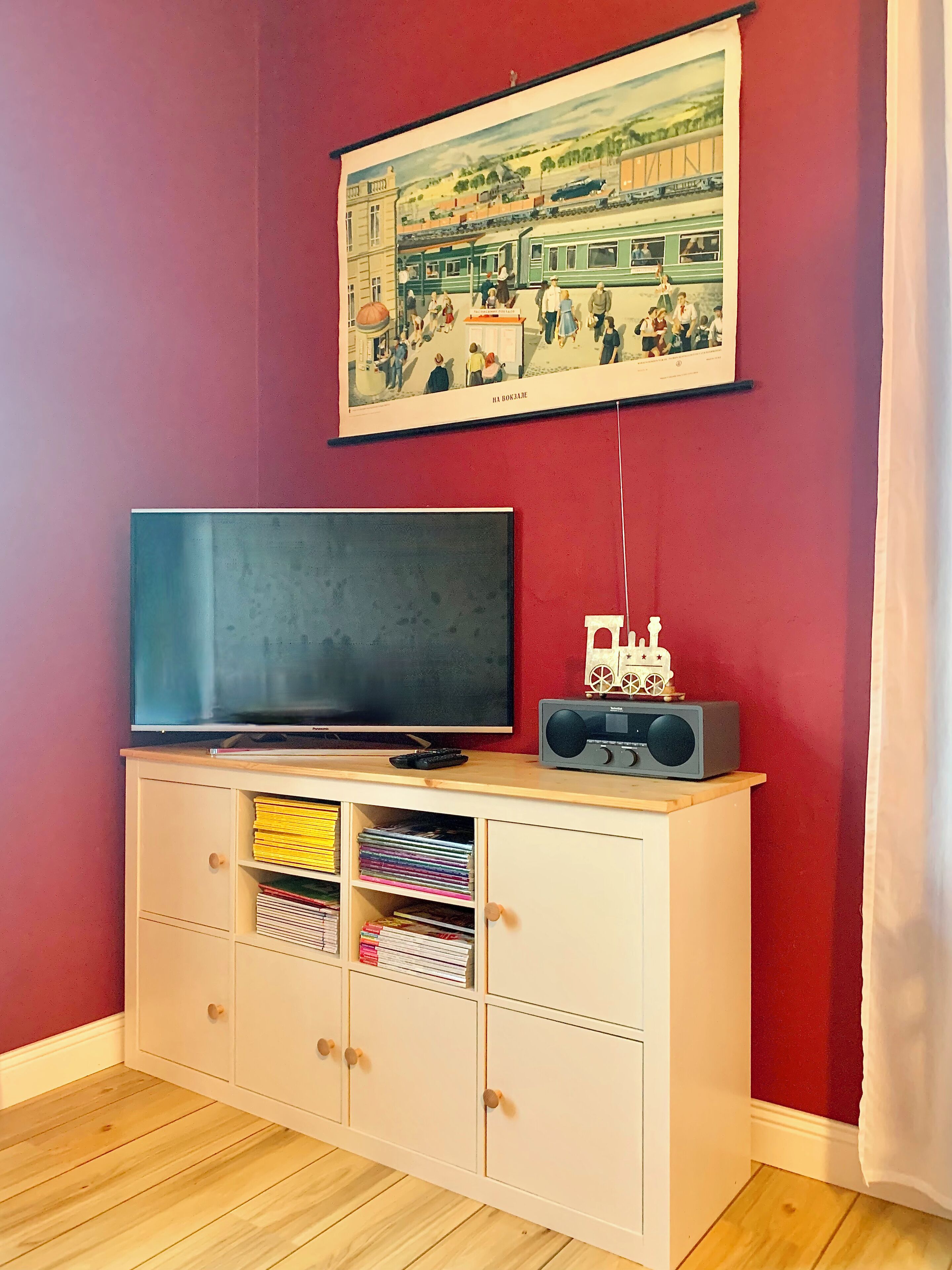 Une pièce avec un téléviseur posé sur un meuble en bois, une radio et un tableau encadré accroché au mur.