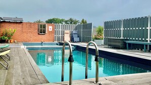 A swimming pool with metal railings, a brick wall, and a wooden deck.