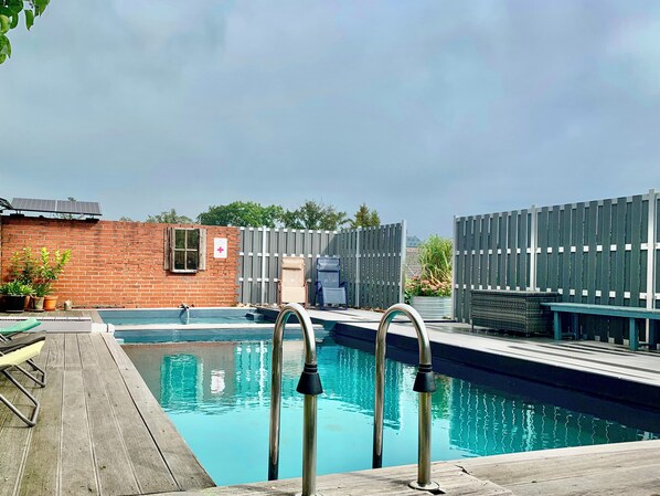 A swimming pool with metal railings, a brick wall, and a wooden deck.