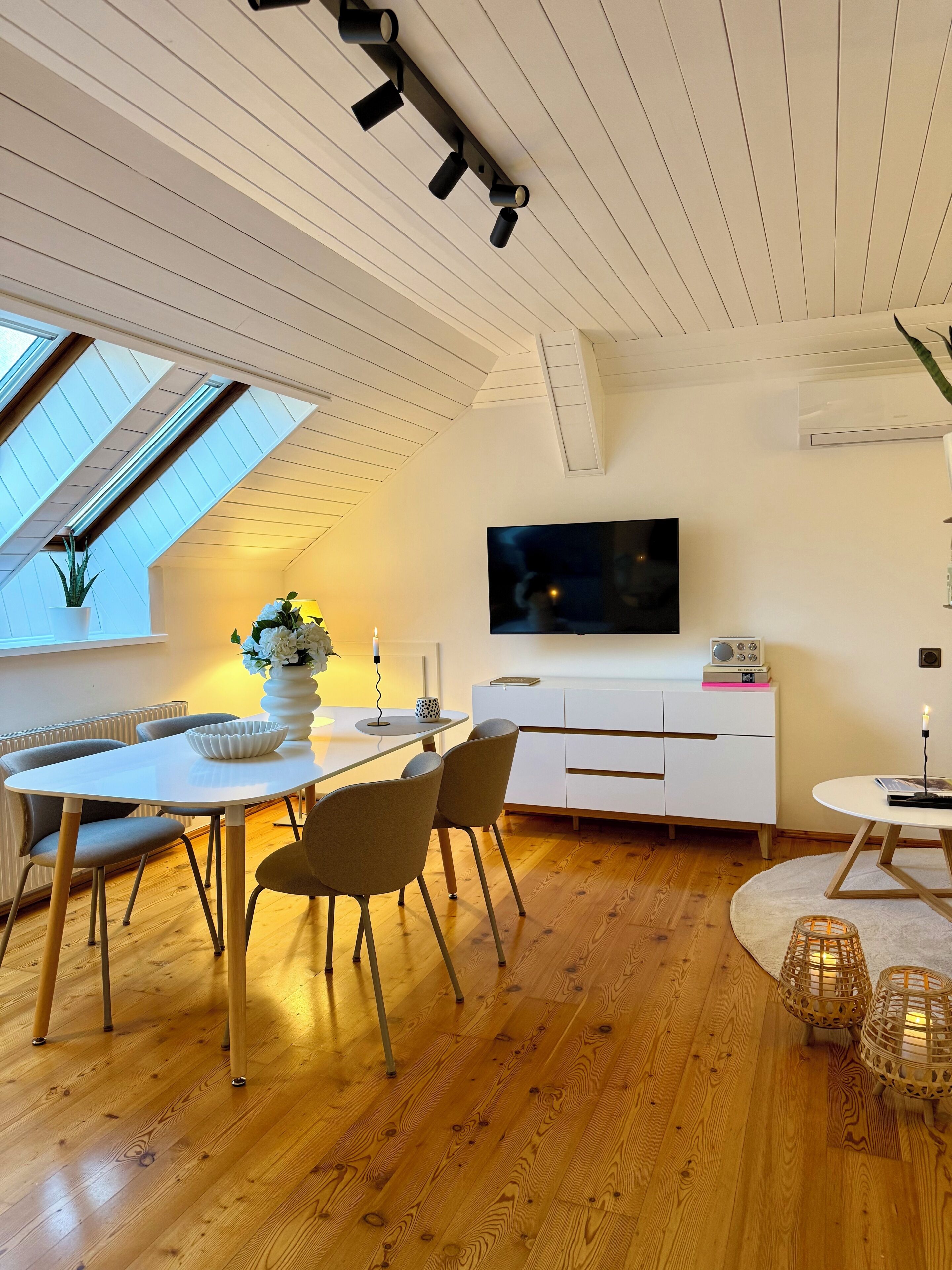 Ein modernes Wohnzimmer mit Essbereich, einem Flachbildfernseher und einem weißen Schrank.