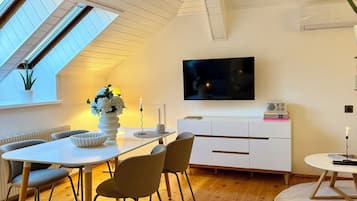 Ein modernes Wohnzimmer mit Essbereich, einem Flachbildfernseher und einem weißen Schrank.