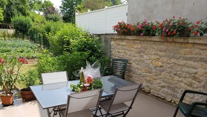 An outdoor patio with a glass table and metal chairs, surrounded by a stone wall and potted plants.