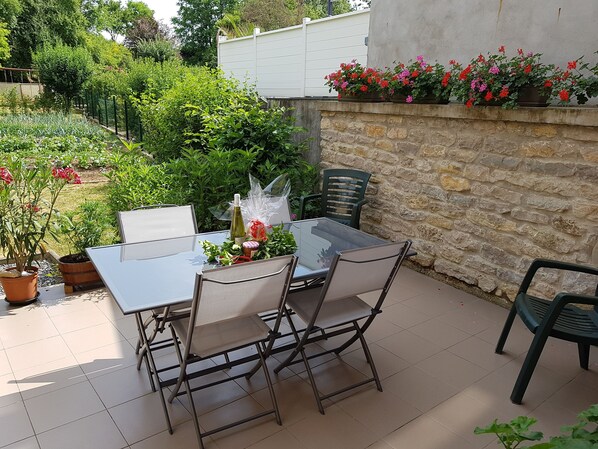 An outdoor patio with a glass table and metal chairs, surrounded by a stone wall and potted plants.
