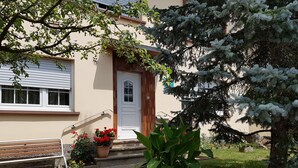 A house with a white door, a wooden bench, and a garden with various plants and flowers.