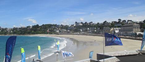 A beach with flags, a sandy shore, and buildings in the background.