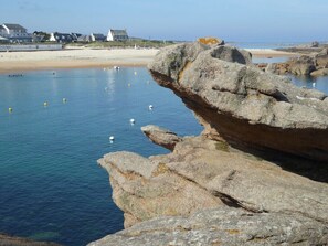A coastal landscape with large rocks, calm water, and a sandy beach.