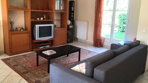 A living room with a grey sofa, a black coffee table, a TV on a wooden stand, and a large window with curtains. - Beautiful house with large garden near Disneyland (Bussy-Saint-Georges)